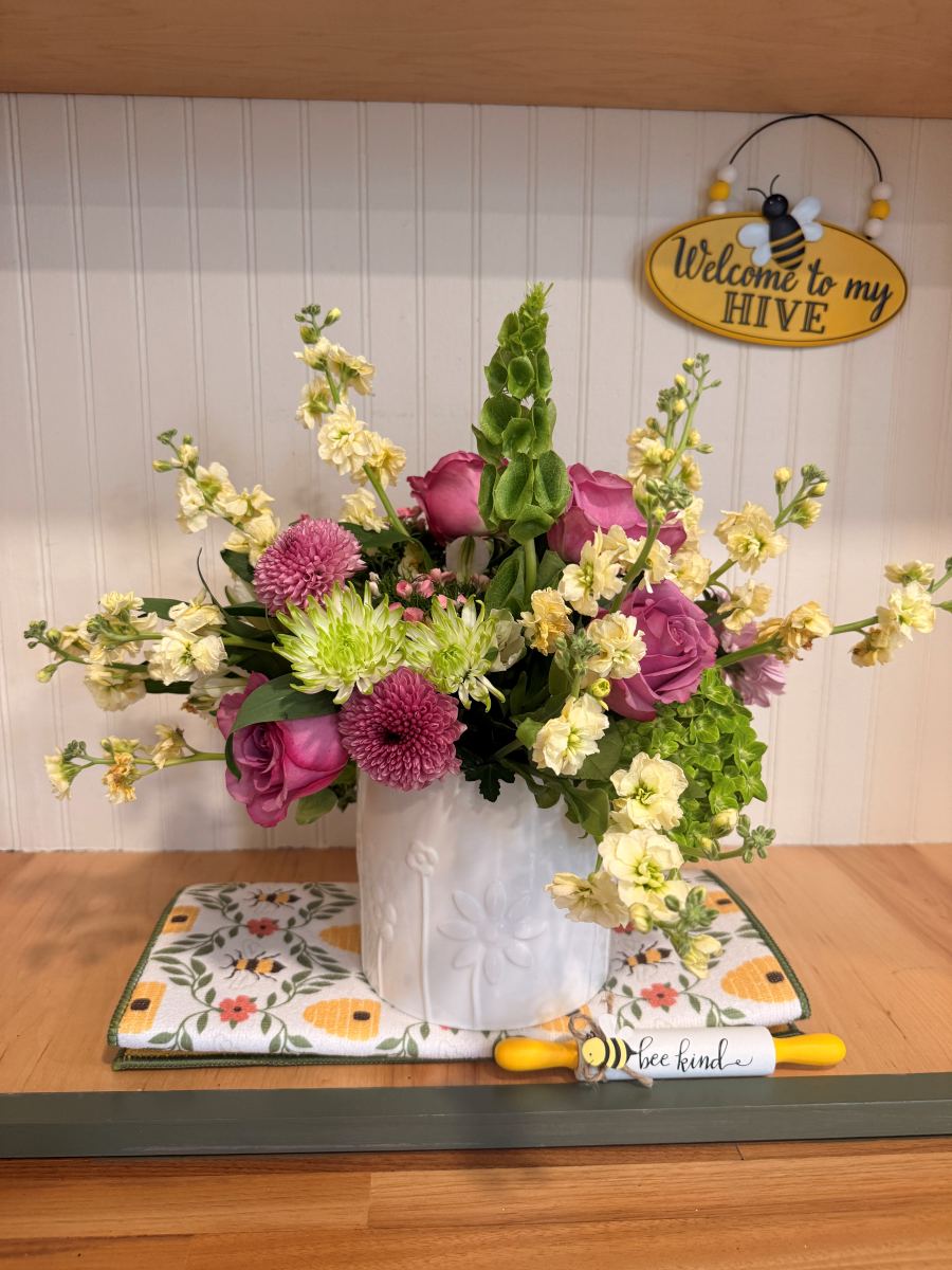 Purple roses and stock beneath a Welcome to my Hive sign