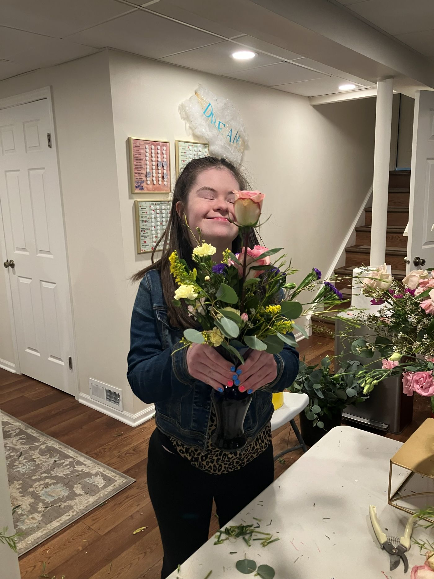 A Be Yourself Flower Shoppe team member smiling with her finished arrangement beneath a hand-lettered DREAM sign